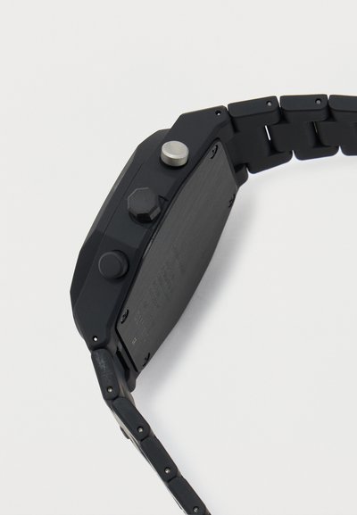 Πλάγια όψη ενός μαύρου ψηφιακού ρολογιού με τρία κουμπιά ελέγχου και μπρασελέ με συνδέσμους σε λευκό φόντο.