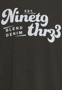 Svart t-skjorte med stor hvit tekst som sier "EST. Ninety thr33" og mindre tekst "BLEND DENIM." Glatt stoff med klassisk passform.