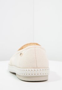Beige canvas instap schoenen met een gestructureerde bovenkant, decoratieve stiknaden en een geweven touwzool. Voorzien van een klein logo-detail aan de zijkant.