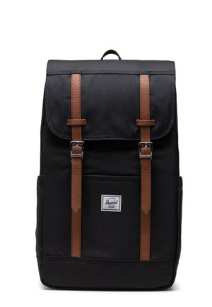 Mustekka canvas-reppu, jossa on ruskeat nahkahihnat ja metalliset soljet, etutasku ja logotunniste pohjassa.