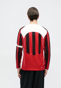 Κόκκινο και μαύρο ριγέ μπλουζάκι με μακριά μανίκια που διαθέτει στρογγυλή πλέξη στην πλάτη, λευκές λεπτομέρειες και εφαρμοστή γραμμή. Το ύφασμα φαίνεται αναπνεύσιμο.