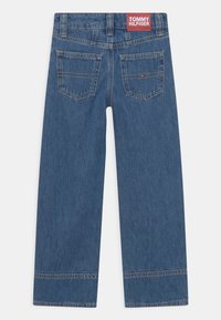 Niebieskie dżinsy z prostymi nogawkami, z czerwoną metką z tyłu oraz dwiema tylniymi kieszeniami z dyskretnymi detalami przeszycia.