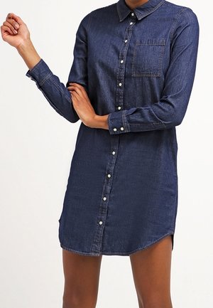 Sukienka koszulowa z denimu w ciemnoniebieskim kolorze, z zapięciem na guziki z przodu, kołnierzem, jedną kieszenią na piersi oraz długimi rękawami z zapinanymi mankietami.