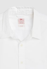 Weiße Slim-Fit-Hemd mit weicher Textur, Button-Down-Kragen und kleinem, aufgesticktem Logo auf der Brust. Etikett zeigt "Levi's Battery Shirt".