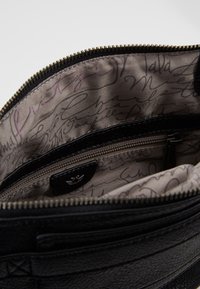 Borsa a tracolla in pelle nera con esterno testurizzato, chiusura con zip e interno foderato caratterizzato da un motivo in stile scritto a mano. Include una piccola tasca con zip.
