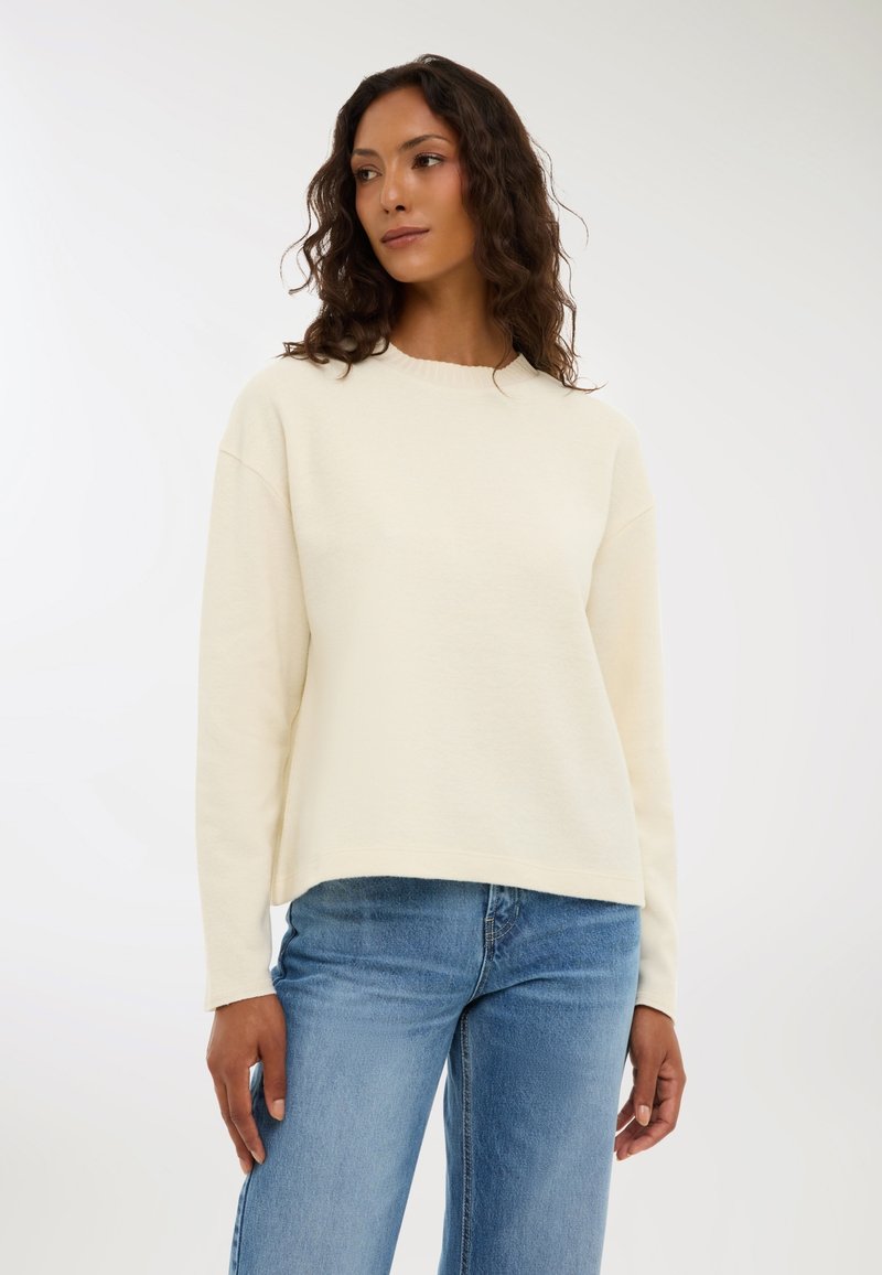 Kremowy, miękki sweter z bawełny o okrągłym dekolcie, długich rękawach i luźnym kroju, połączony z jasnoniebieskimi dżinsami.