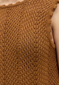 Gros plan d'un haut marron en crochet sans manches avec un bord festonné porté sur une épaule nue.