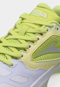 Κοντινό πλάνο ενός κίτρινου και λευκού αθλητικού παπουτσιού με υφασμάτινα πάνελ με υφή, χοντρές κορδόνια και λογότυπο στην γλώσσα και την πλευρά.