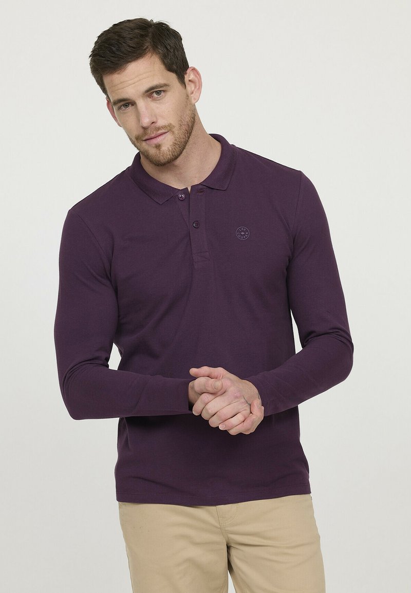 Polo à manches longues en coton violet profond, avec un col, une patte de boutonnage à trois boutons et un logo discret sur la poitrine.