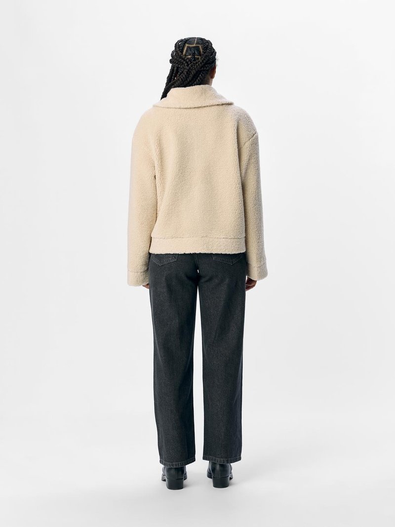 Beżowa bluza z polaru z zamkniętym kołnierzem, krótkim krojem i teksturowanym materiałem, zestawiona z ciemnymi spodniami straight-leg oraz botkami za kostkę.