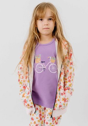 Young girl with long blonde hair wearing a floral jacket and pants, and a purple shirt with a bicycle and flower baskets print.
