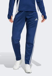 Marineblaue Sporthose mit weißen Seitenstreifen, aus glattem, dehnbarem Material. Mit Reißverschlussabschlüssen und einem Adidas-Logo auf dem Oberschenkel.