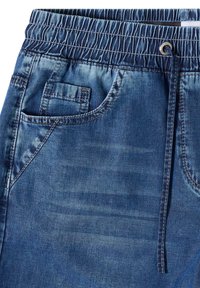 Pantalon bleu denim avec taille élastique, poches avant, petite poche pour pièces, et cordon noir noué à la taille.