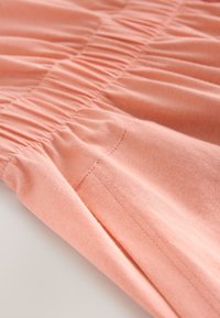 Tissu rose doux avec couture élastique froncée créant un effet froncé le long de la couture sur une surface lisse.