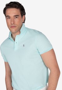 Camisa polo de color azul claro con mangas cortas, cuello con solapa y logo bordado en el lado izquierdo del pecho. Fabricada con un tejido suave y transpirable.