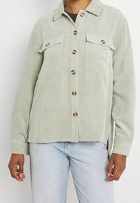 Ljusgrön kordjacka med krage, långa ärmar, knappstängning fram, två bröstfickor och en avslappnad passform. Har bruna knappar.