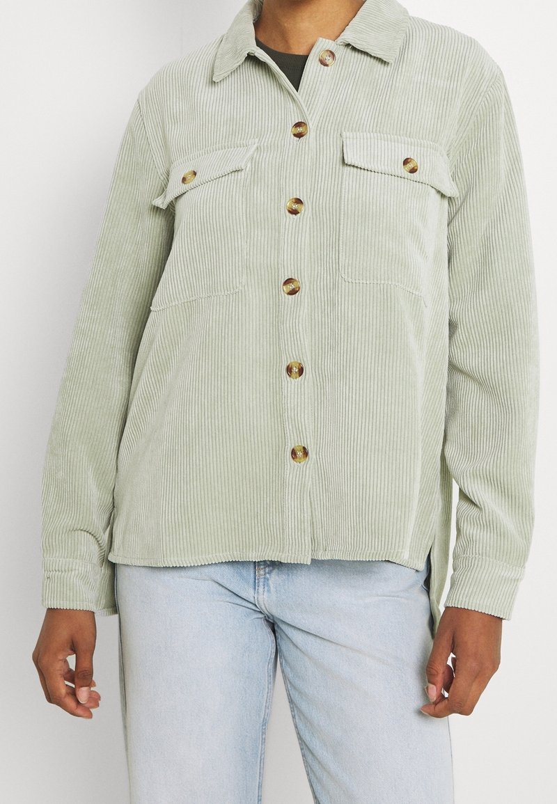 Ljusgrön kordjacka med krage, långa ärmar, knappstängning fram, två bröstfickor och en avslappnad passform. Har bruna knappar.