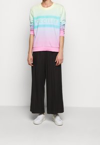 Pastellfärgad sweatshirts med en rundad halsringning, med ordet "CECILIE" centralt placerat; ihop med löst sittande svarta byxor och vita sneakers.