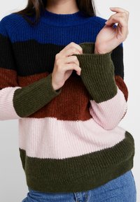 Sweter dziergany z wyraźnymi poziomymi paskami w kolorach niebieskim, czarnym, brązowym, zielonym, ciemnoróżowym i jasnoróżowym, z prążkowaną fakturą i mankietami.