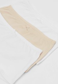 Drei Paar Baumwollslips in Weiß und Nude, mit elastischen Bündchen und kleinen Schleifen. Glatte Textur, schlichtes Design.