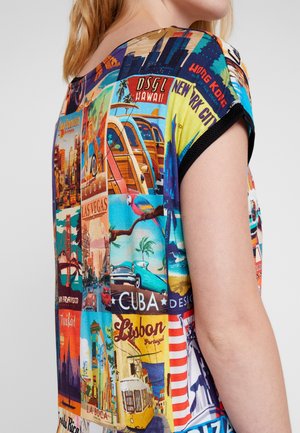 Kvinde iført en farverig kortærmet top med vintage rejseplakater af byer som San Francisco, Cuba, Lissabon og New York City.