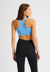 Sujetador deportivo azul con tirantes anchos y ajustables y una textura suave, combinado con leggings negros de cintura alta que presentan un sutil detalle de costura.