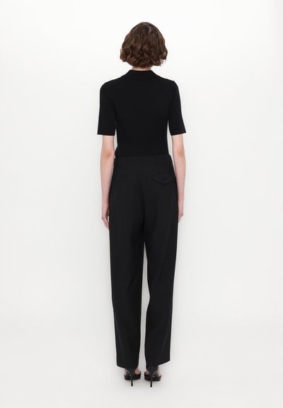 Haut noir ajusté à manches courtes, associé à un pantalon noir taille haute avec un détail de poche arrière et une texture lisse.