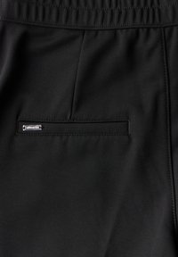 Černé sportovní kalhoty s elastickým pasem, hladká tkanina, obsahující malou, horizontální kapsu s metalickým akcentem blízko pasu.