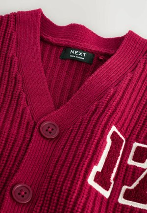 Bordeauxfarbener, gestrickter Cardigan mit tiefem V-Ausschnitt, ausgestattet mit zwei dunklen Knöpfen und einem weißen Akzent mit der Nummer "17" auf der linken Seite. Markenetikett sichtbar.