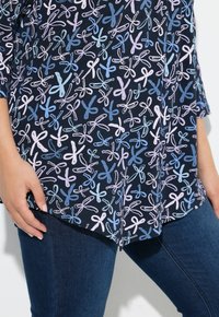Marineblauw top met een all-over strikprint in lichtblauw en roze. Kenmerkt zich door een afgeronde zoom en driekwartmouwen, gemaakt van zachte stof.