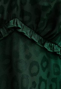 Tela de estampado de leopardo verde con textura suave, que presenta un dobladillo fruncido. El patrón es sutil sobre el fondo verde oscuro.