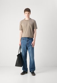 Tann kortermet t-skjorte med logo, blå straight-leg jeans, svart lærveske og mørke sneakers. Enkelt design, uformell stil.