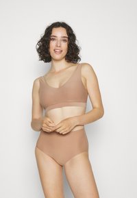 Lichtbruine naadloze bralette en hooghangende slipjes, gemaakt van zachte stof. Heeft een ronde halslijn en een brede, elastische band.
