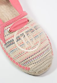 Zapato de esparto tejido en crema con rayas multicolores. Presenta acentos de tela rosa y un logo bordado circular en el costado.