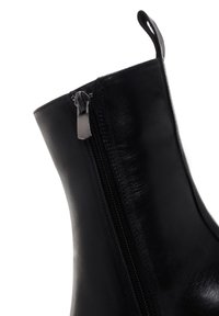Stivale alla caviglia in pelle nera con zip laterale e linguetta nella parte superiore su sfondo bianco.