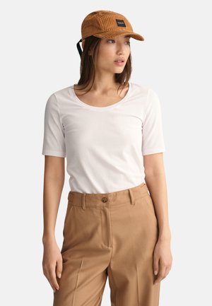 Vit kortärmad topp med rund hals som är kombinerad med ljust bruna högmidjade byxor, som har en subtil textur och en knappdetalj fram.