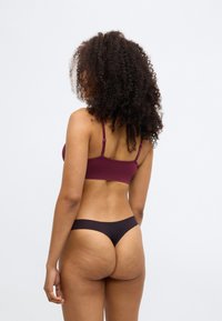 Bralette bordeaux escuro com alças ajustáveis e uma textura suave. Combinado com uma tanga roxa profunda, de cobertura mínima e design elegante.