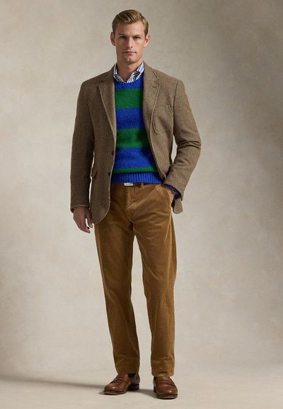 Blondeman met een bruine pied-de-poule blazer, een blauw-groene gestreepte trui, een gestreept overhemd, bruine corduroy broek en bruine leren schoenen.