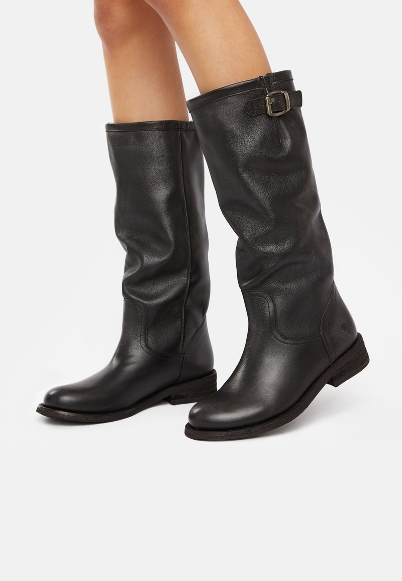 Black leather knee-high boots with a slightly slouched design, prominent stitching, and a buckle accent on the collar. Flat wooden sole.