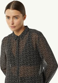 Black sheer blouse featuring a repeating white geometric pattern, a pointed collar, button closure, and long sleeves with a relaxed fit.