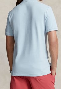 Ljusblå bomullspolo med korta ärmar och krage, med en mjuk textur; bärs tillsammans med korallfärgade shorts.