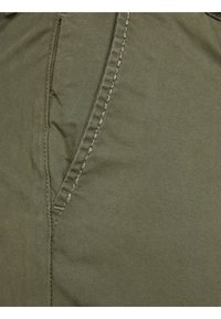 Primer plano de una tela verde oliva con una textura suave, con costuras claras en contraste a lo largo de la costura y un diseño de bolsillo lateral en ángulo.