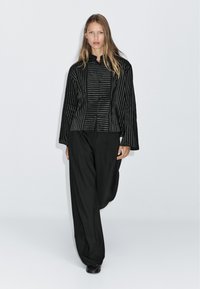 Giacca a strisce nere con chiusura a bottoni e maniche ampie, abbinata a pantaloni neri larghi. L'insieme presenta un design elegante e moderno.