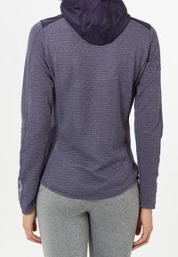 Lila långärmad hoodie med textilstruktur och en lätt huva. Har accentpaneler på axlarna och en förlängd nederkant på ryggen.