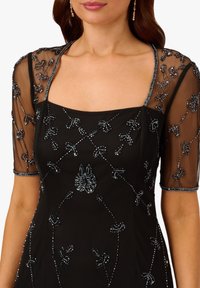 Schwarzes Kleid mit transparenten, verzierten Ärmeln. Geschmückt mit kunstvollen Blumenmustern, quadratischem Ausschnitt und einer figurbetonten Silhouette.