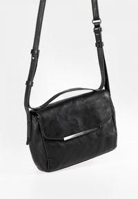 Zwarte leren schoudertas met een klepsluiting en zilverkleurige hardware, met een gestructureerd oppervlak en een verstelbare riem.