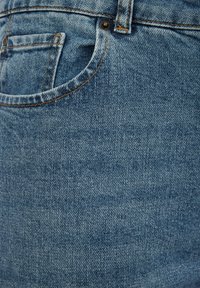 Tela de mezclilla azul que presenta un primer plano de un bolsillo con accesorios de hardware de cobre y costuras en contraste, mostrando una superficie texturizada.