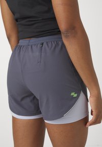 Dameidrettsshorts i mørkegrå med innebygget lys grå fôr. Har elastisk midjebånd og en sidelomme med glidelåsdetalj.