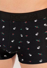 Boxer-briefs en coton noir avec un motif présentant des têtes de mort blanches et des roses rouges. Taille élastique avec texte en relief.