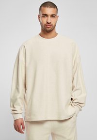 Lichtbeige lange mouwen ribben shirt met een ronde halslijn, losse pasvorm en omgeslagen mouwen. Zachte textuur, minimalistisch ontwerp.